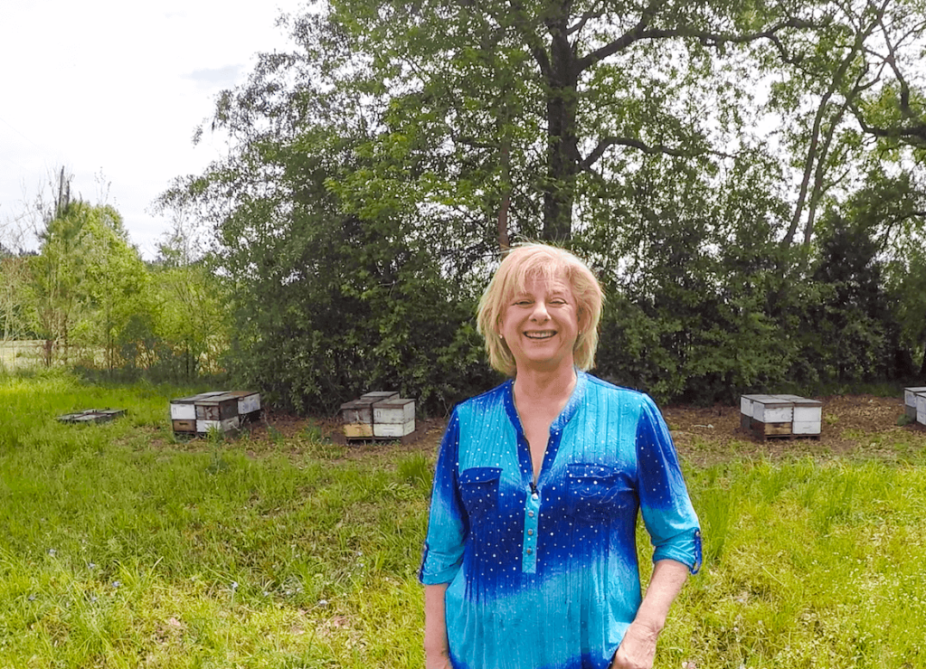 A photo of Beekeeper Jane Collins standing in front of beehives in her bee yard.