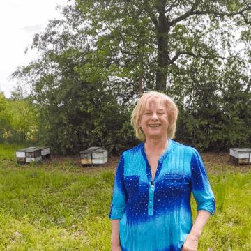 A photo of Beekeeper Jane Collins standing in front of beehives in her bee yard.