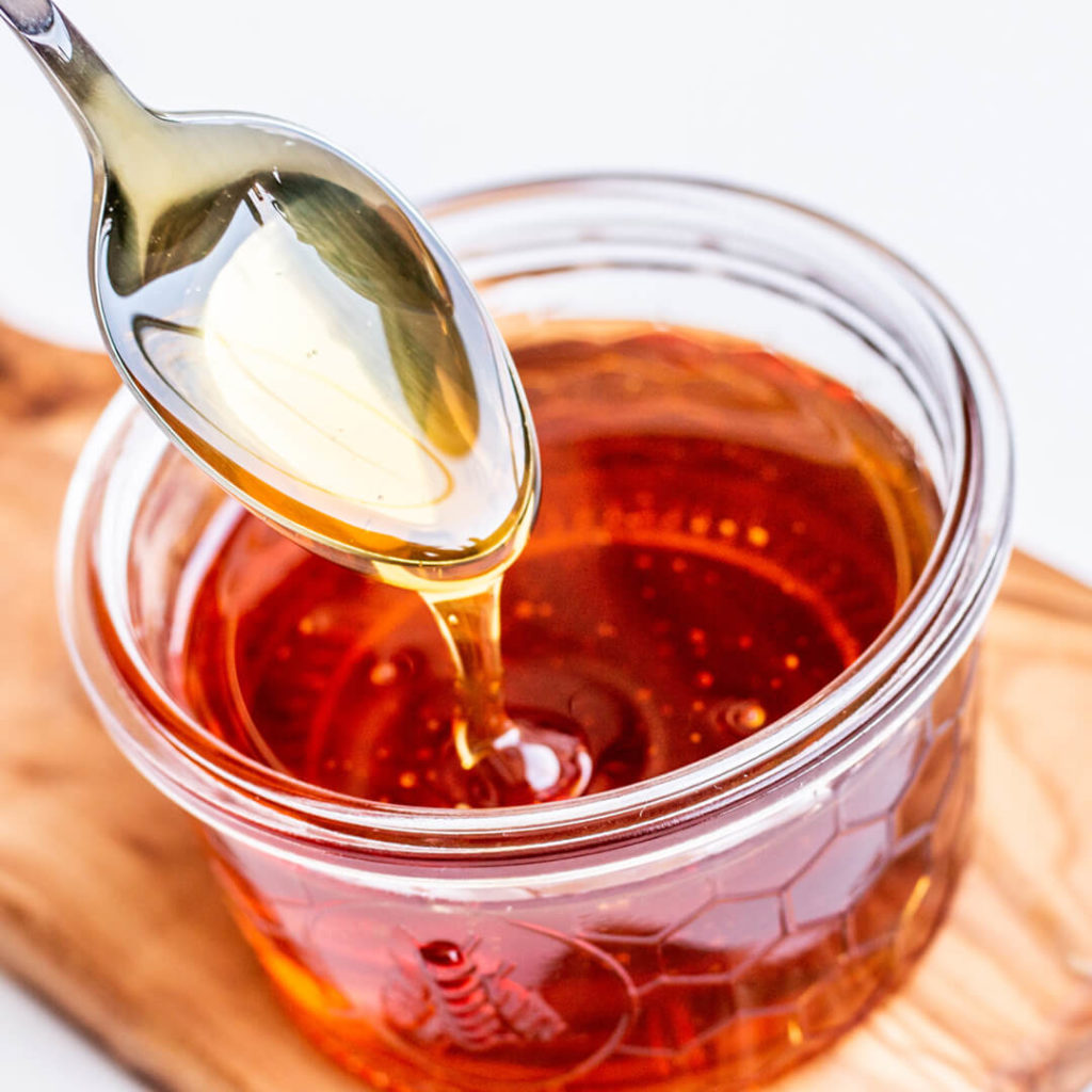 Photo of honey pouring from a spoon into a jar of honey.
