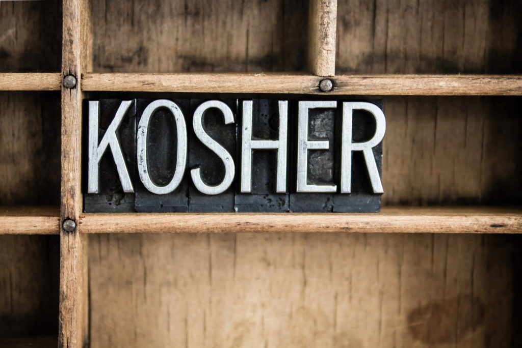 The word "KOSHER" written in vintage metal letterpress type in a wooden drawer with dividers.